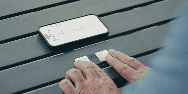 Person using KardiaMobile device with a smartphone displaying an EKG reading